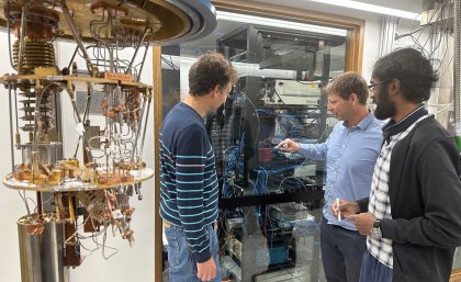 AQC researchers working on maths equations on glass wall with gold plated fridge in foreground. Image UQ 